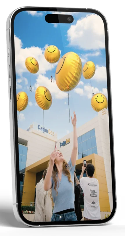 Kampanya görseli telefon ekranında: hastane önünde gökyüzüne uçan gülen yüzlü sarı balonlar